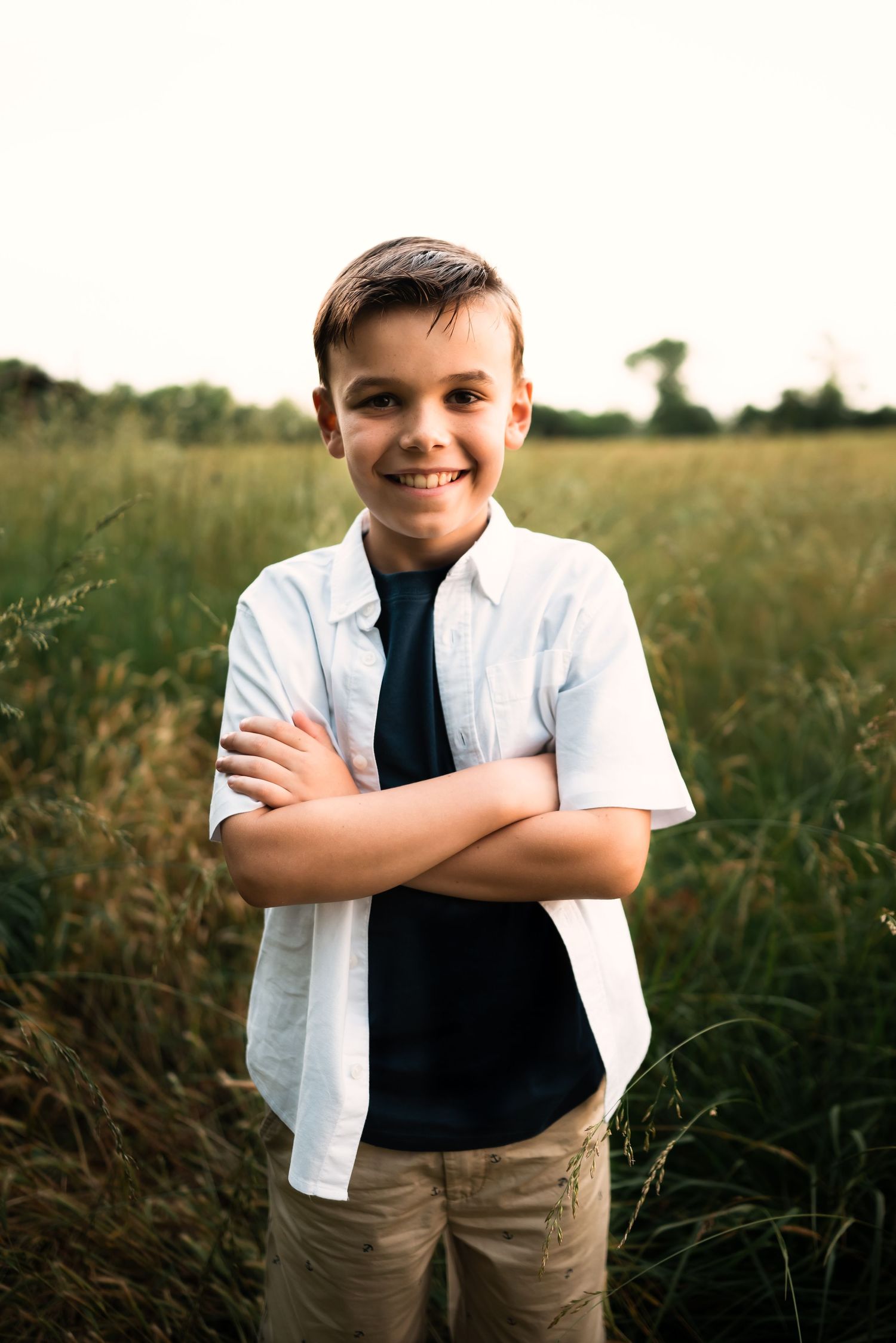 A young person in a white shirt and tie poses confidently in a grassy field.