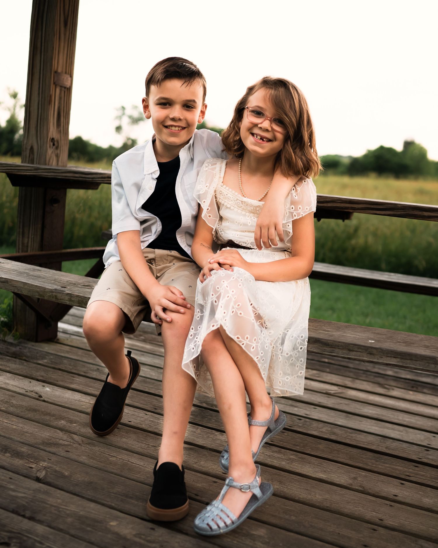 Siblings sharing playful moment on wooden deck at sunset.