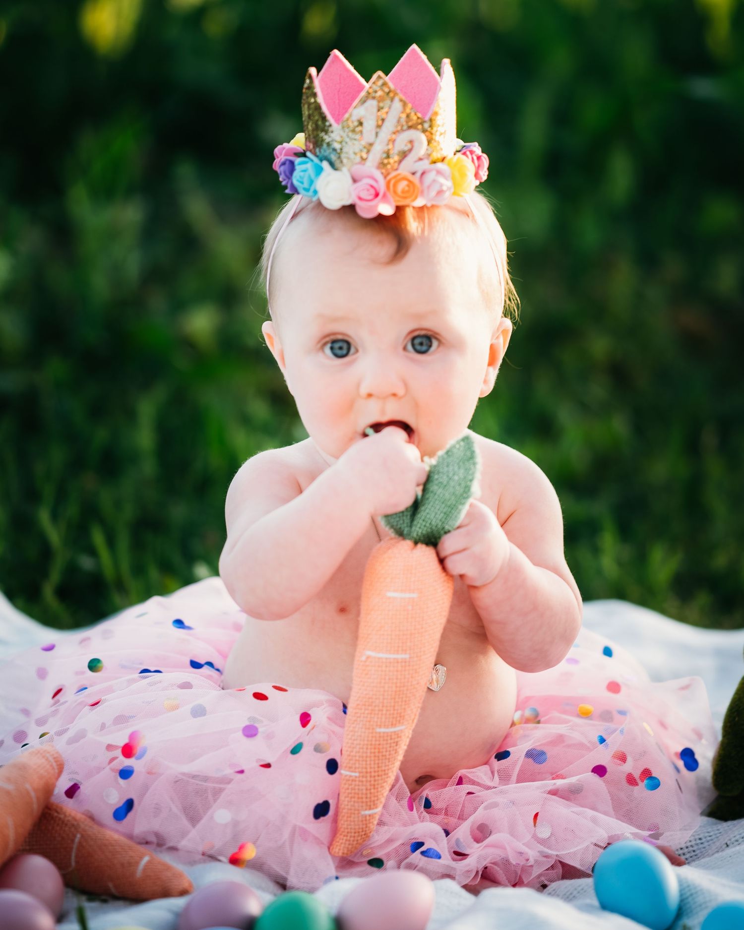 Baby in pink tutu dress plays with colorful toys on outdoor deck.