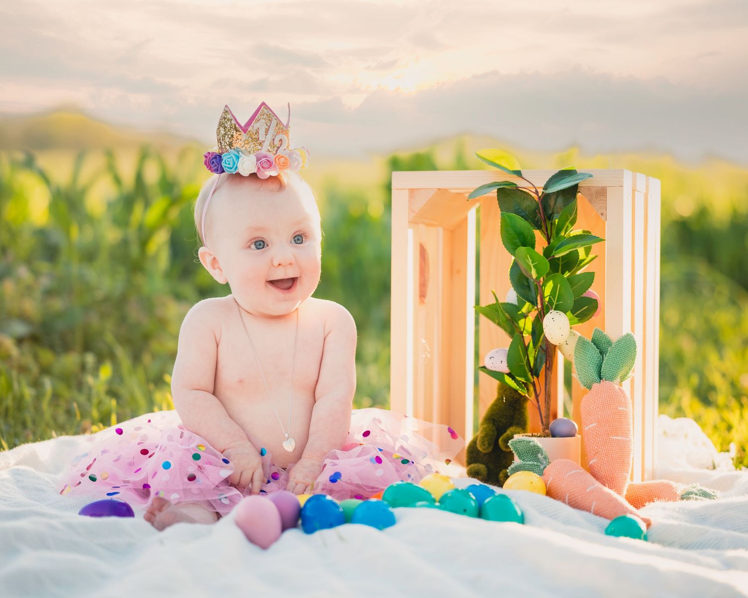 Baby in pink tutu poses with colorful decorations in outdoor setting.