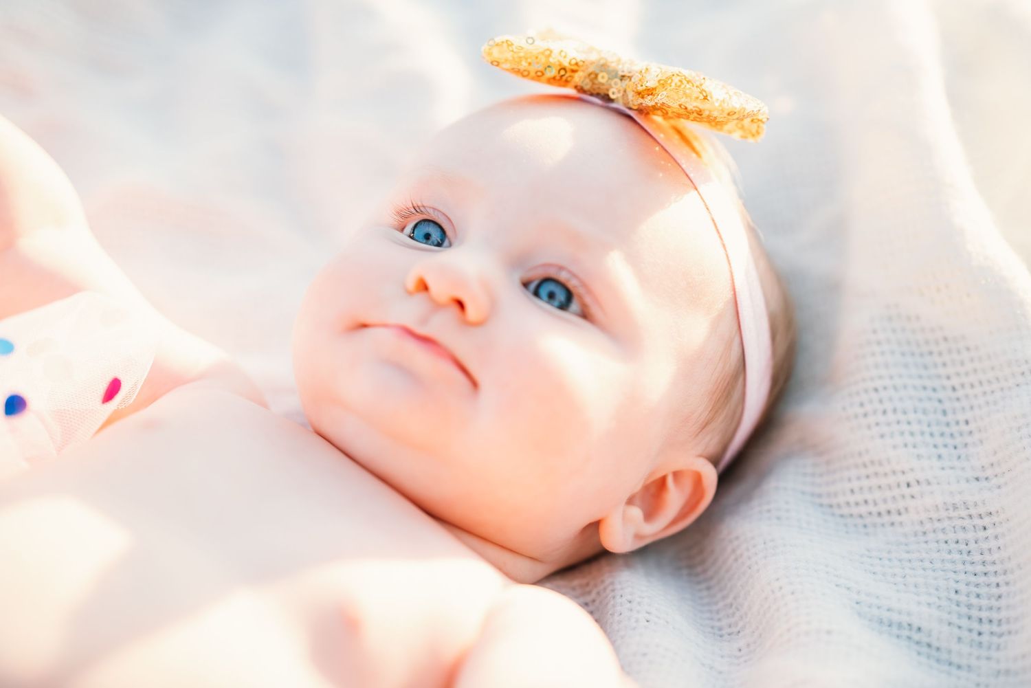 Close-up portrait of baby wearing pink bow against soft background.