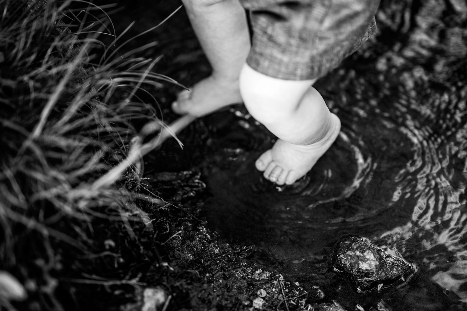Black and white image of small feet stepping in puddle or water.