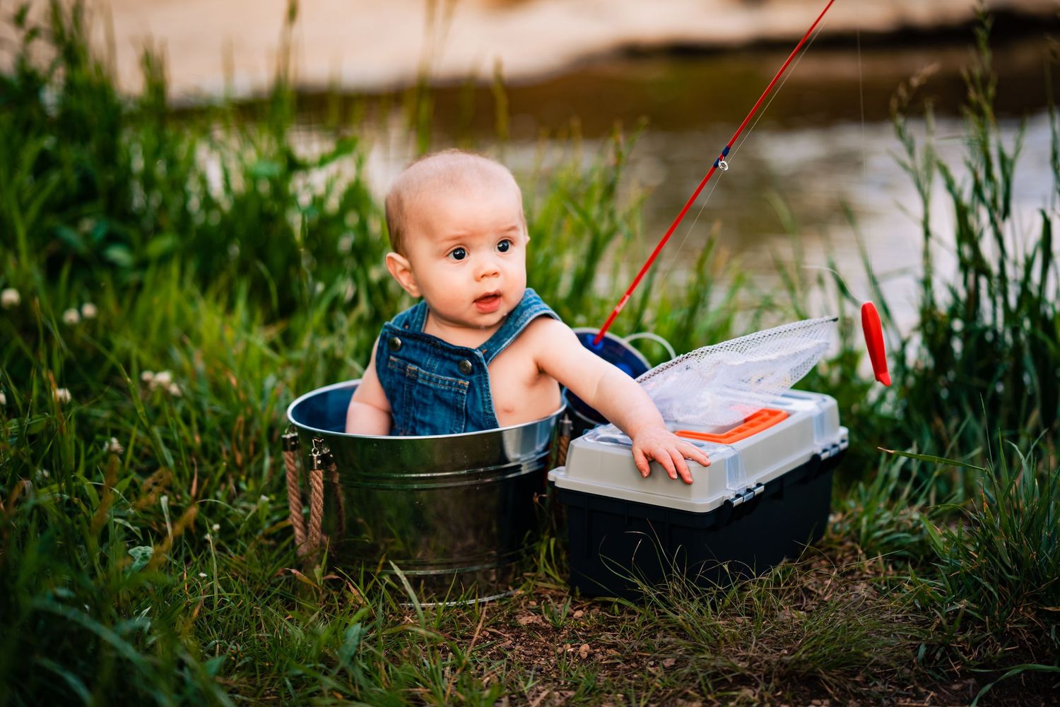 Baby plays in vintage metal washtub surrounded by greenery.