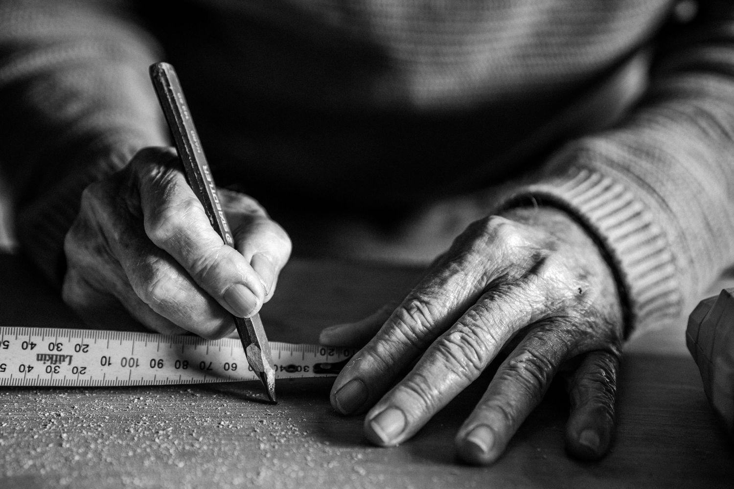 Hands of an elderly man taking a measurement on a piece of wood.