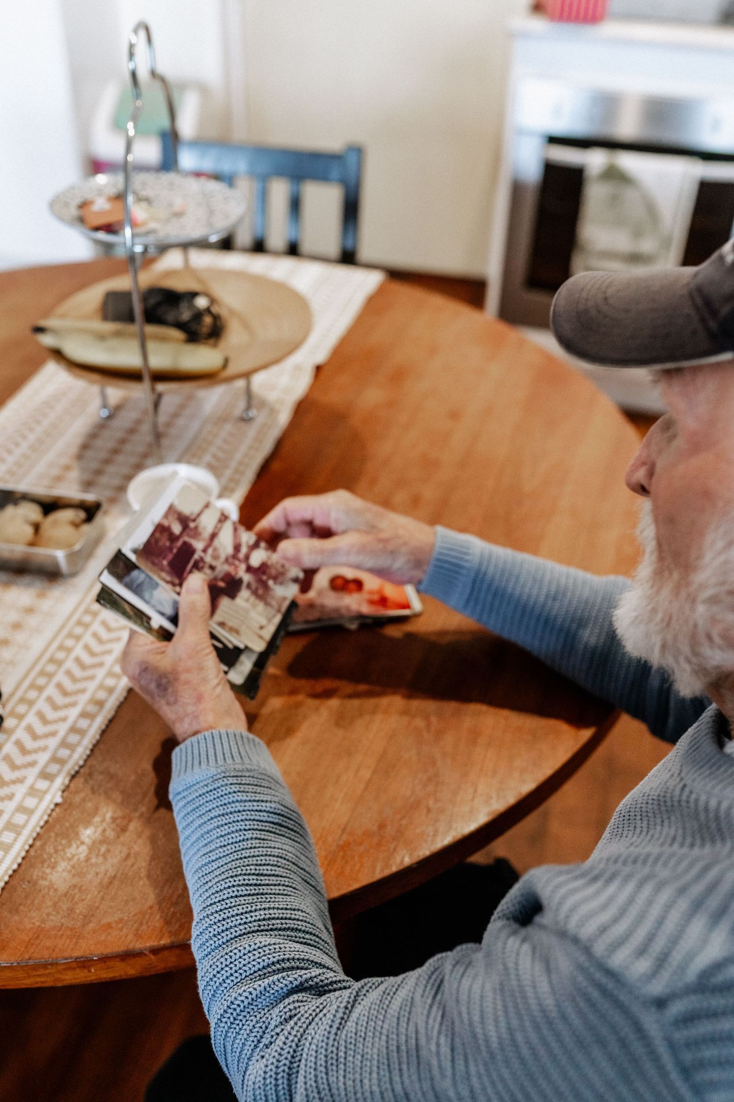 An elderly man sits at a dining table looking through a collection of old photos.
