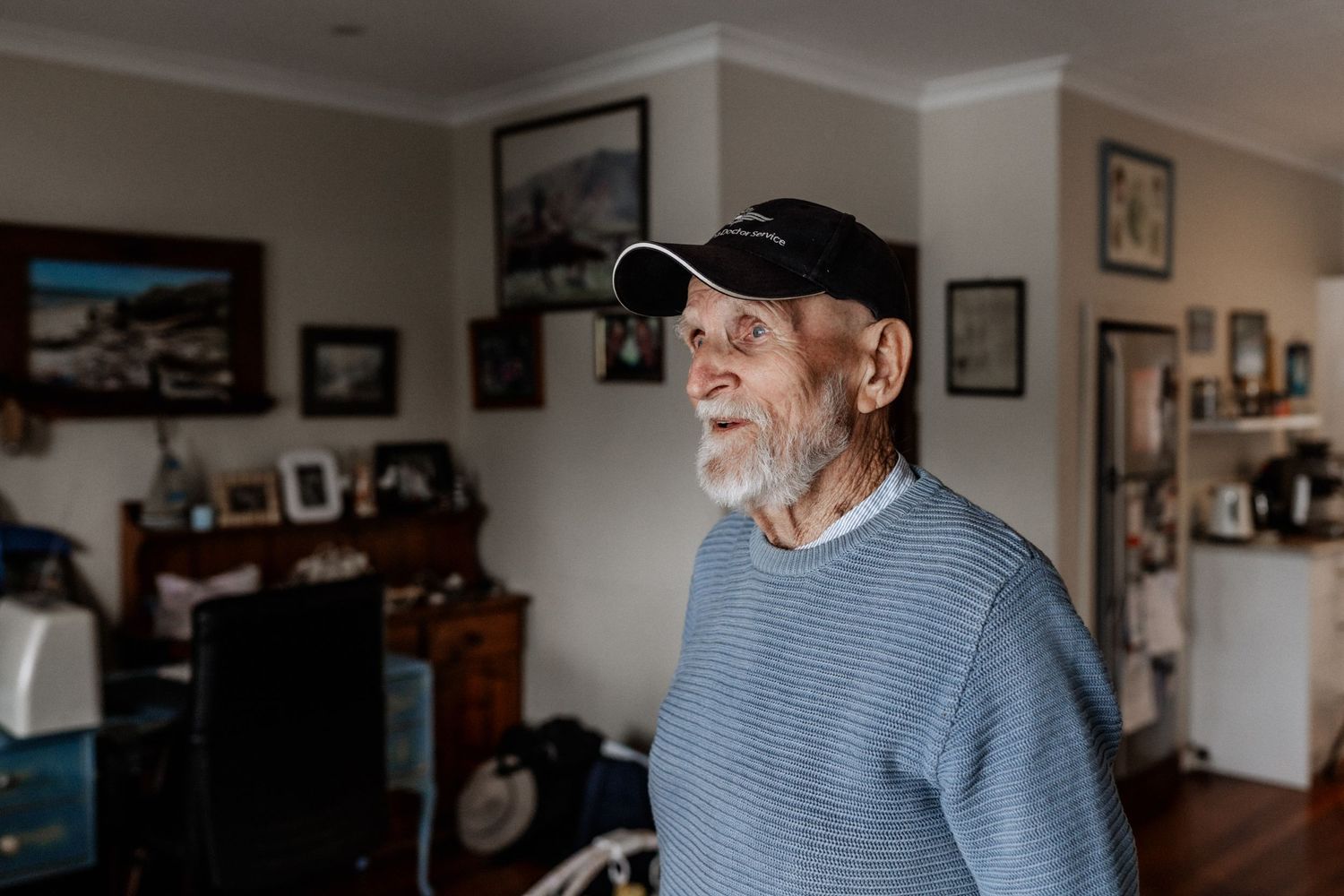 An elderly man gazes out of a lounge room window.