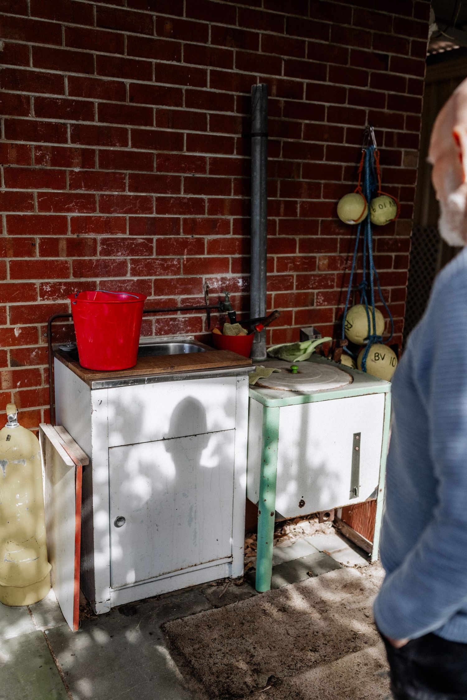 The shadow of an elderly man falls on an outdoor trough and washing up area.