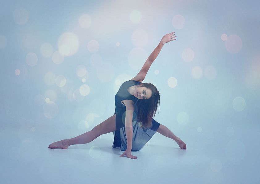 Contemporary dancer in blue leotard performing graceful movement on light blue background with bokeh effects.