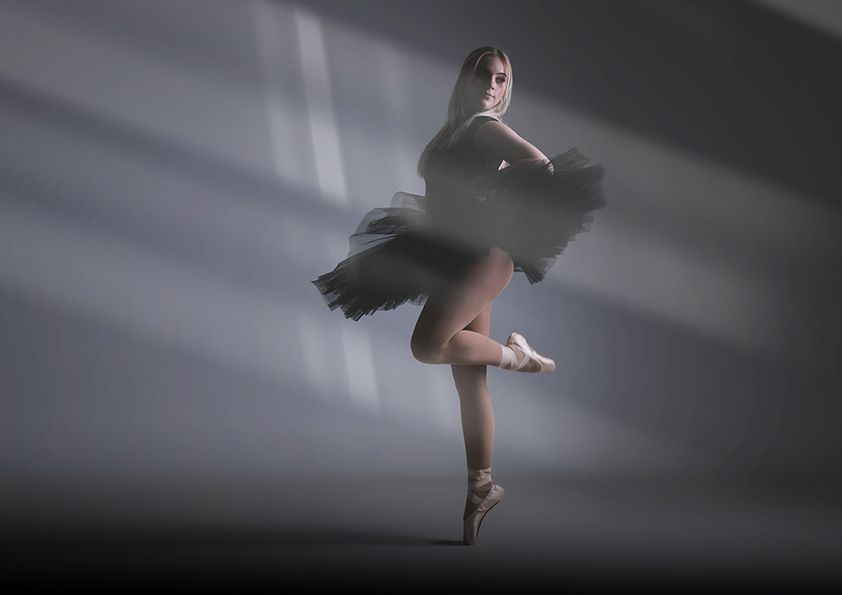 Ballerina in black tutu performs graceful spin pose in dramatic lighting against dark background.