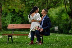 A couple sits together on a wooden bench in a lush green park setting during a romantic spring day.
