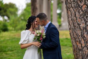 A romantic wedding moment captured outdoors with a bouquet of pink flowers, against a natural park setting.