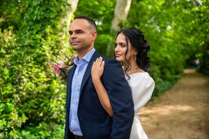 A couple stands together on a scenic garden path surrounded by lush green foliage during a wedding photoshoot.