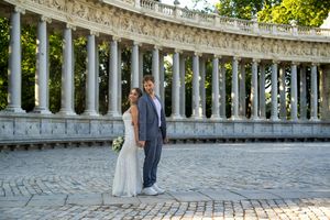 A couple in wedding attire stands in front of ornate white stone columns at Retiro Park in Madrid, Spain.