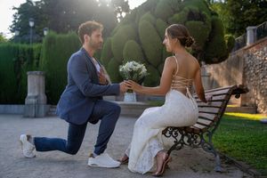 A couple shares an intimate moment on a garden bench during a sunset proposal with white flowers.