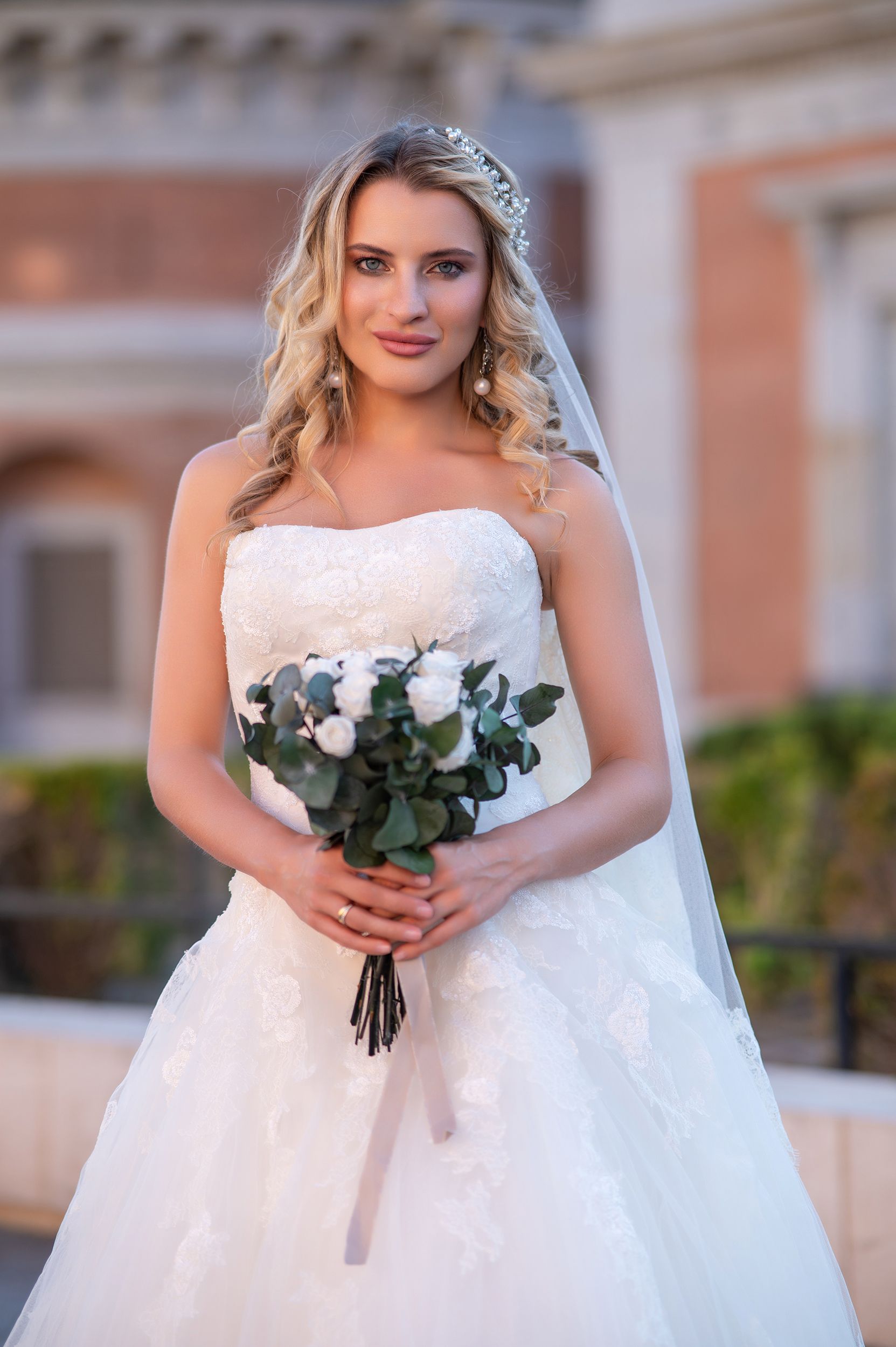 Beautiful bride in white lace wedding gown holding a eucalyptus bouquet while wearing a crystal tiara and veil.