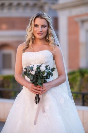 Beautiful bride in white lace wedding gown holding a eucalyptus bouquet while wearing a crystal tiara and veil.