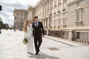 A bride and groom walk hand in hand along the exterior of Madrid's Royal Palace on their wedding day.