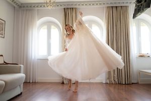 A flowing white dress twirls in an elegant room with arched windows and beige curtains.