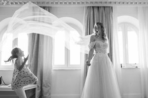 Black and white photo of a wedding dress flowing in a room with arched windows.