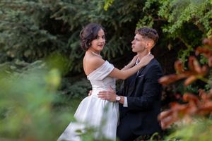 A couple in wedding attire embraces in a romantic garden setting with lush greenery in the background.