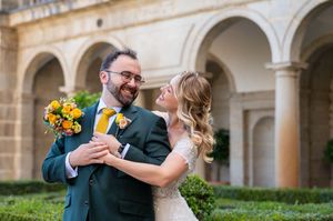 Couple embraces and laughs together in an elegant courtyard with stone archways and columns.