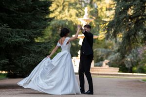 A couple in wedding attire dances together in a lush garden setting during golden hour.