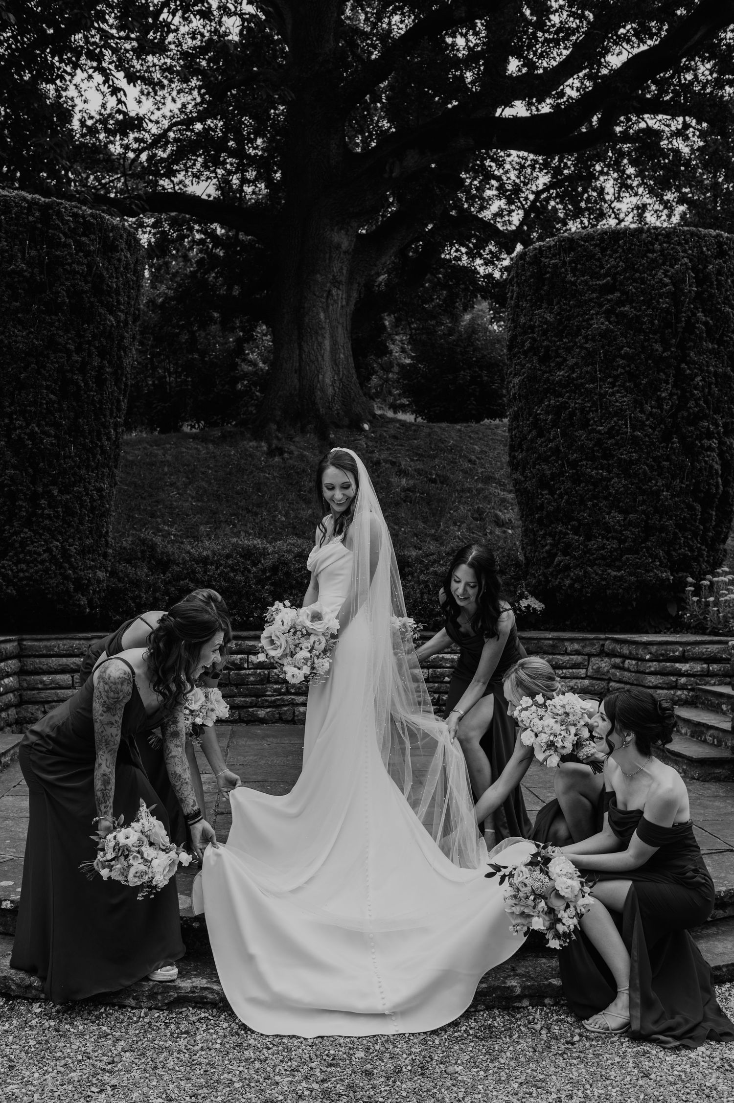 Black and white photo sequence showing bridesmaids helping adjust a bride's flowing wedding dress train outdoors.
