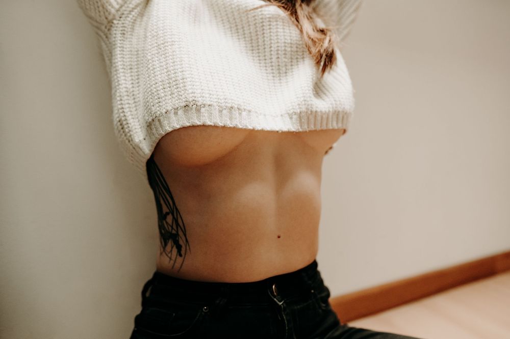 Woman in white cropped sweater poses in front of neutral wall showing different angles and poses.