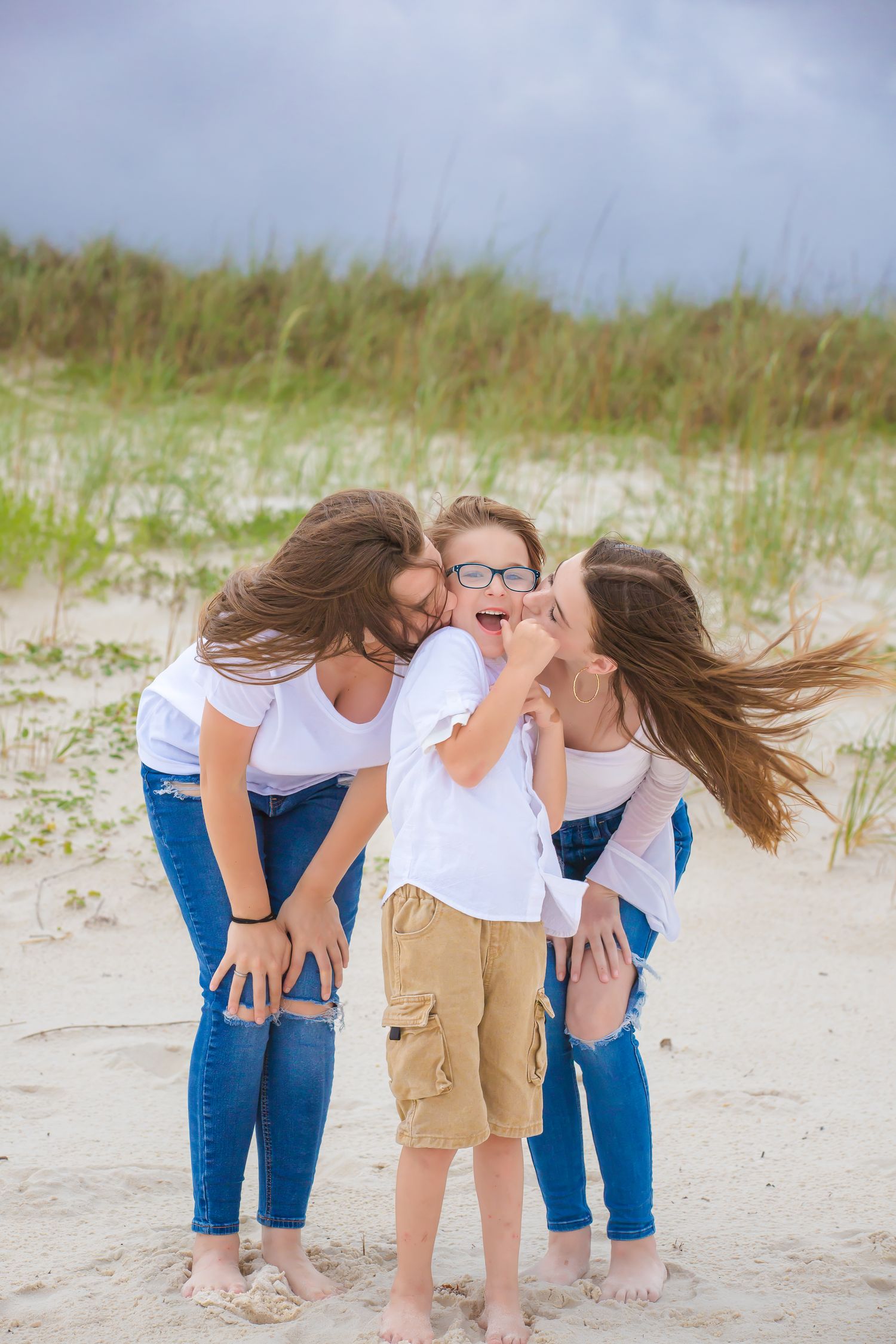 Sweet candid moment of affection captured on sandy beach with dune grass in background.