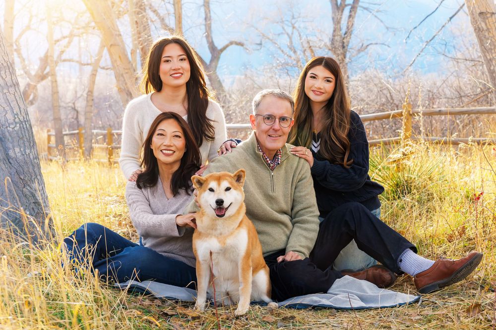 Group relaxes on blanket in autumn field with happy Shiba Inu dog during outdoor photoshoot.