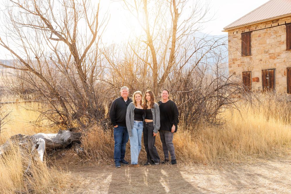 A group stands together on a dirt path near bare winter trees and an old stone building at sunset.
