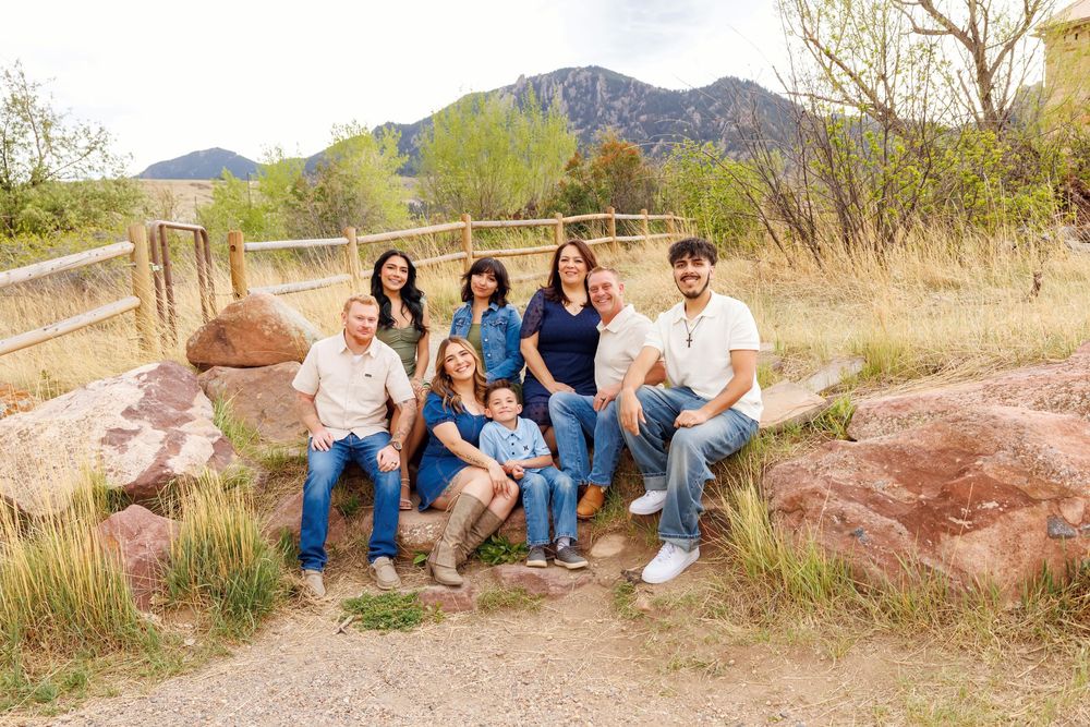 Family portrait of eight people posing on rocks outdoors with mountains and green trees in background.