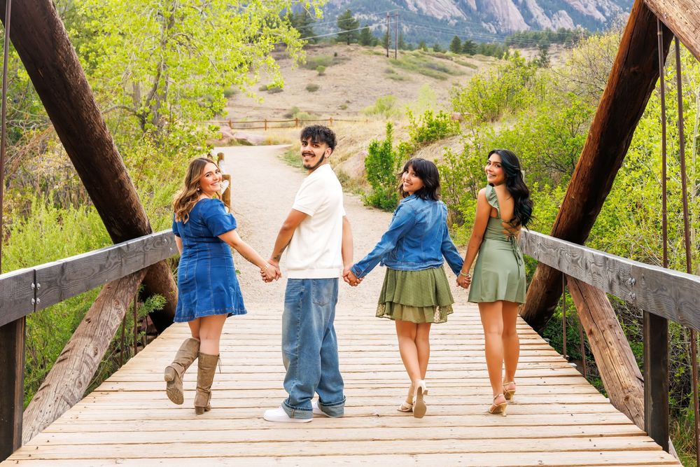 Family of four walks on a wooden bridge in Colorado foothills, holding hands in casual blue and green outfits.