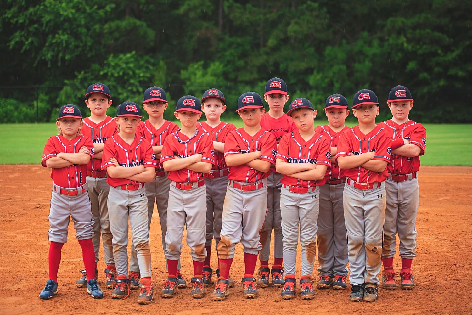 Youth baseball team in red uniforms poses together on dirt field during game day.
