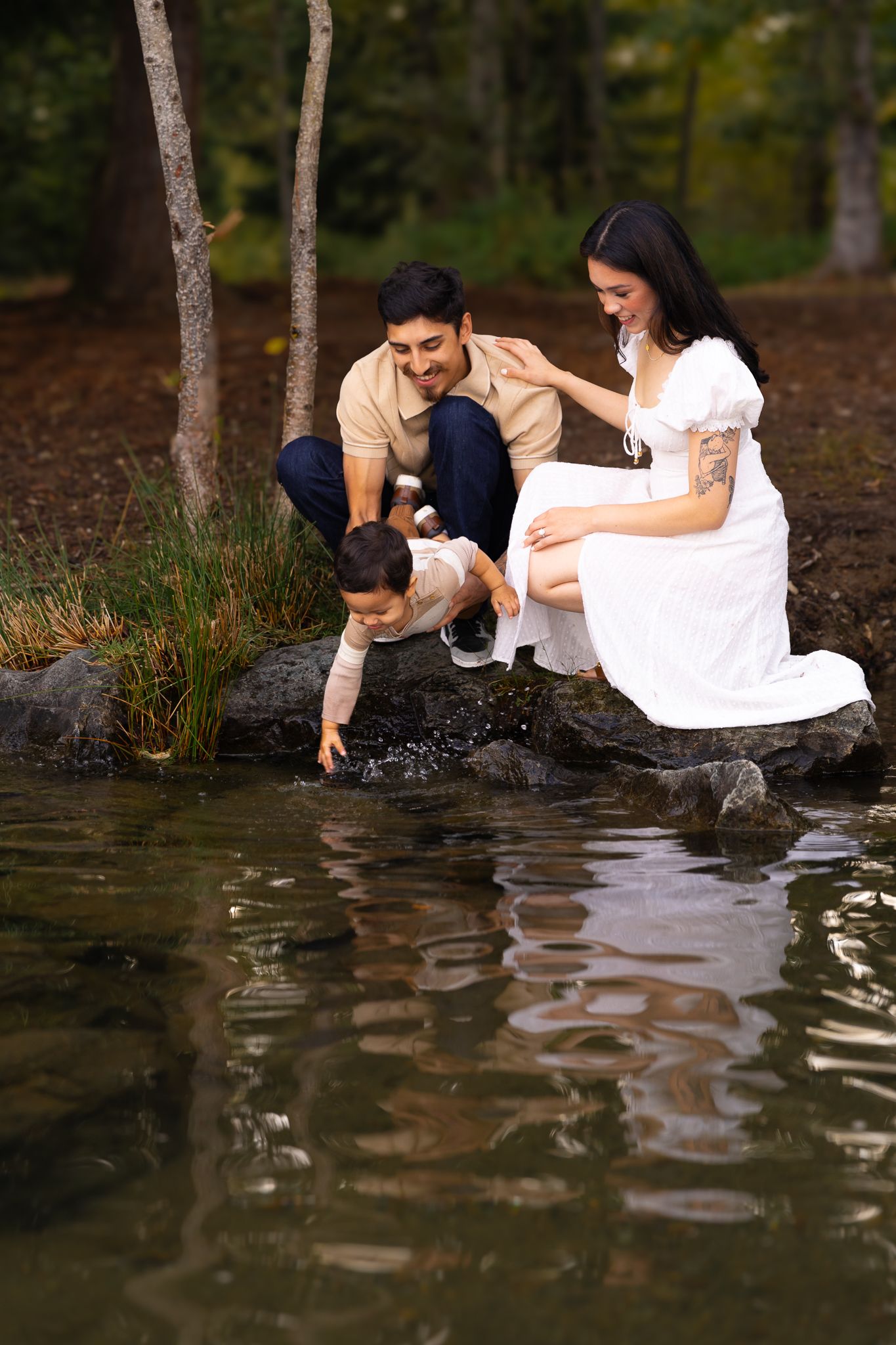 A smiling couple hold their toddler son over Lake Tapps as he reaches for the water during a family lake session in Washington.