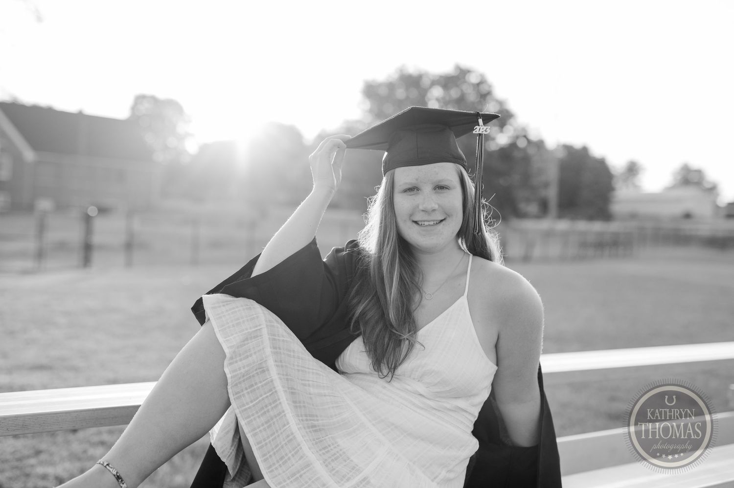 Graduate in cap and gown sitting casually on bleachers in black and white photography.