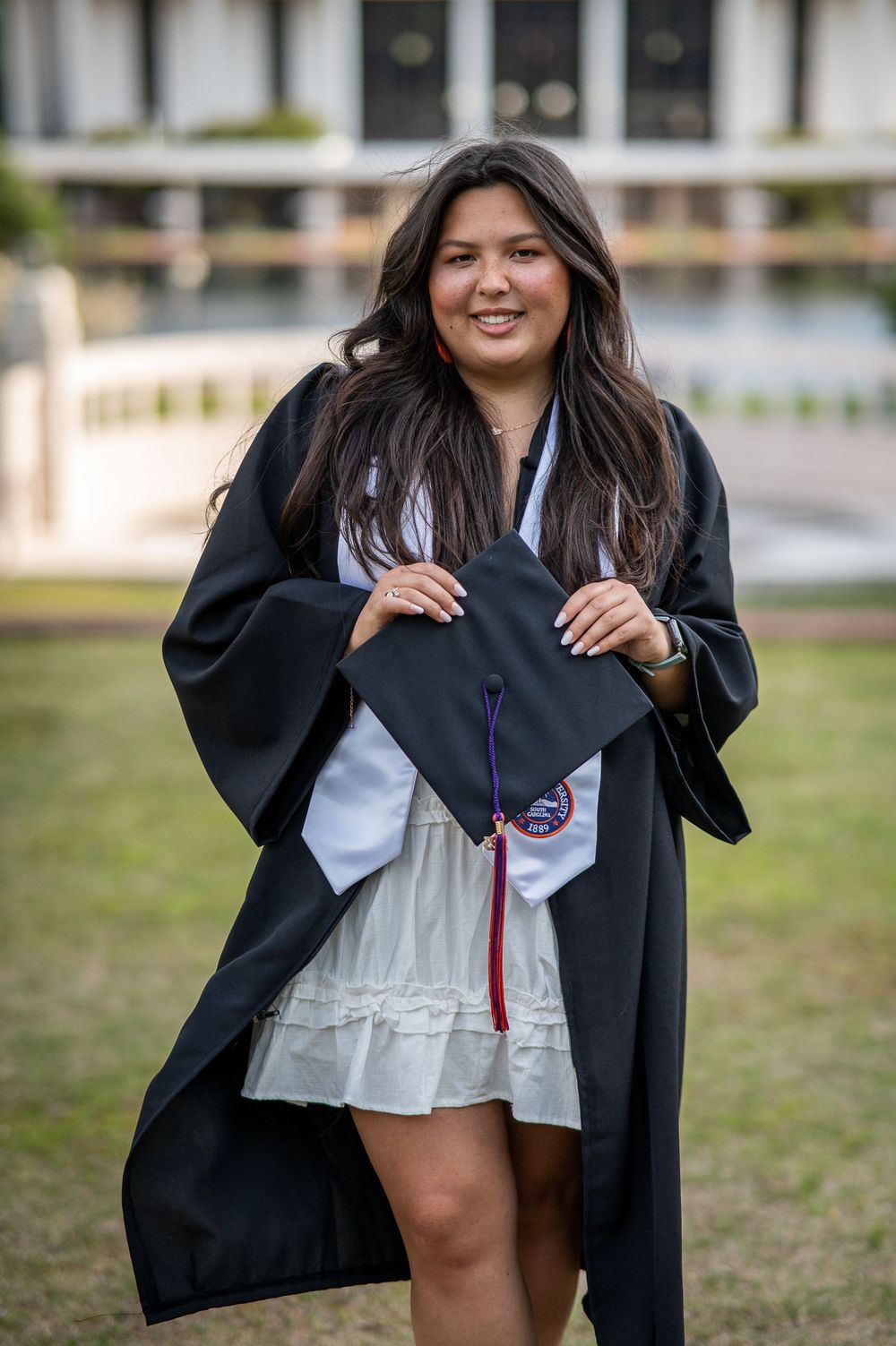 Clemson Graduate in gown holding cap with Cooper Library in the background, Clemson, South Carolina.