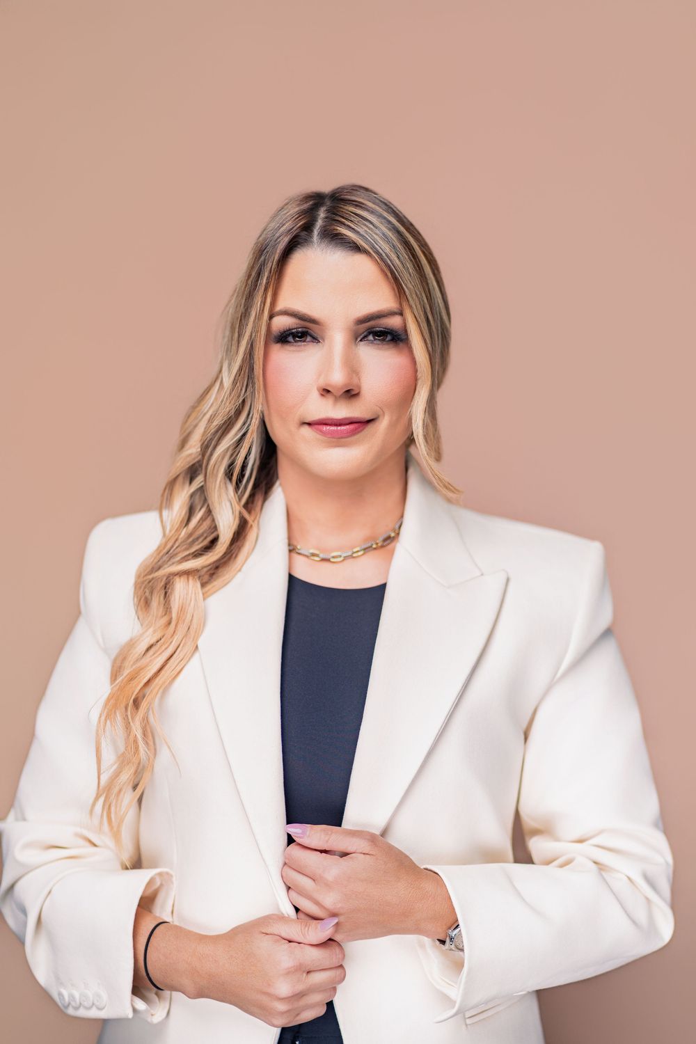Professional portrait of someone in a crisp white blazer and navy top against a neutral background.