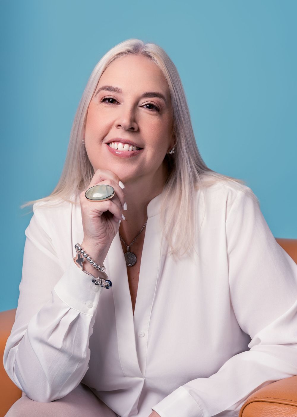 Professional in white blazer smiling in portrait against blue background.