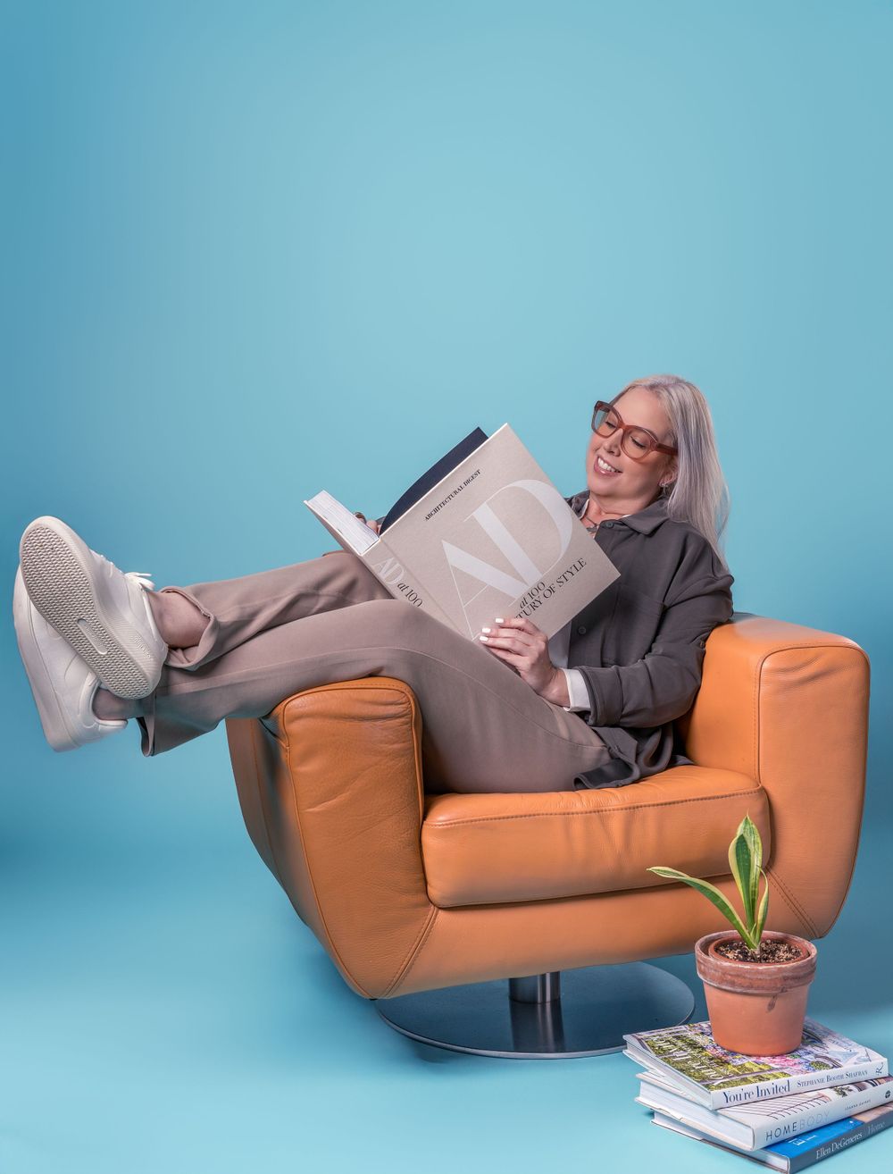Lifestyle photos of someone relaxing on an orange couch with books and plants against blue wall.