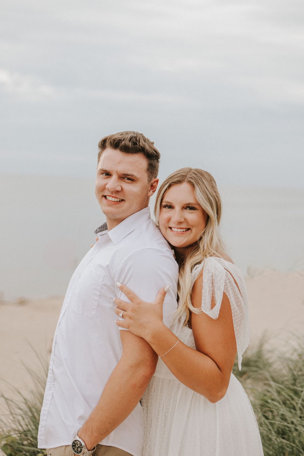 A couple embraces and laughs together on a cloudy beach.