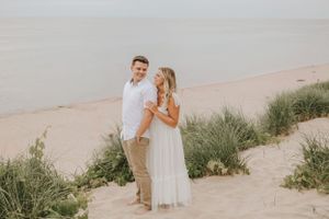 A couple poses for engagement photos on a scenic beach with dune grass.