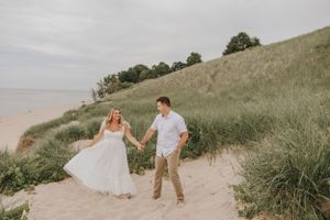 A couple shares a joyful moment while walking on a scenic beach path with dunes.