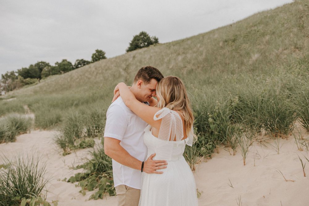 A couple in white clothing sharing an intimate moment on sandy dunes.