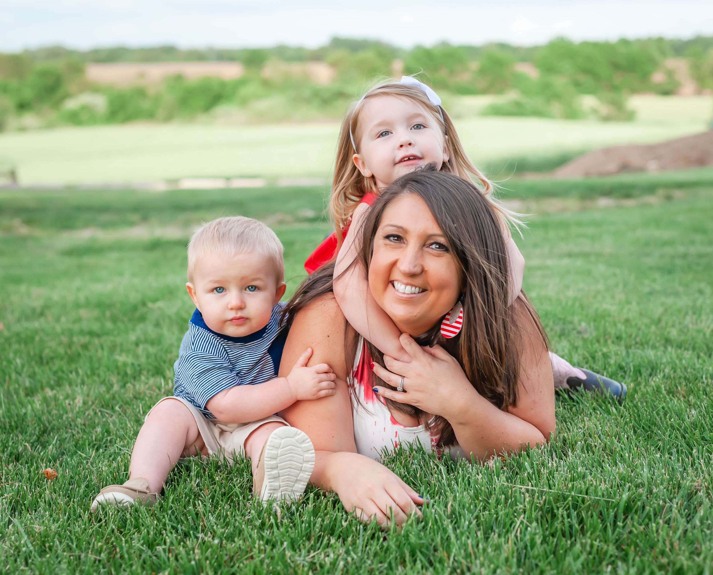 Family members laying together on green grass during a sunny day.
