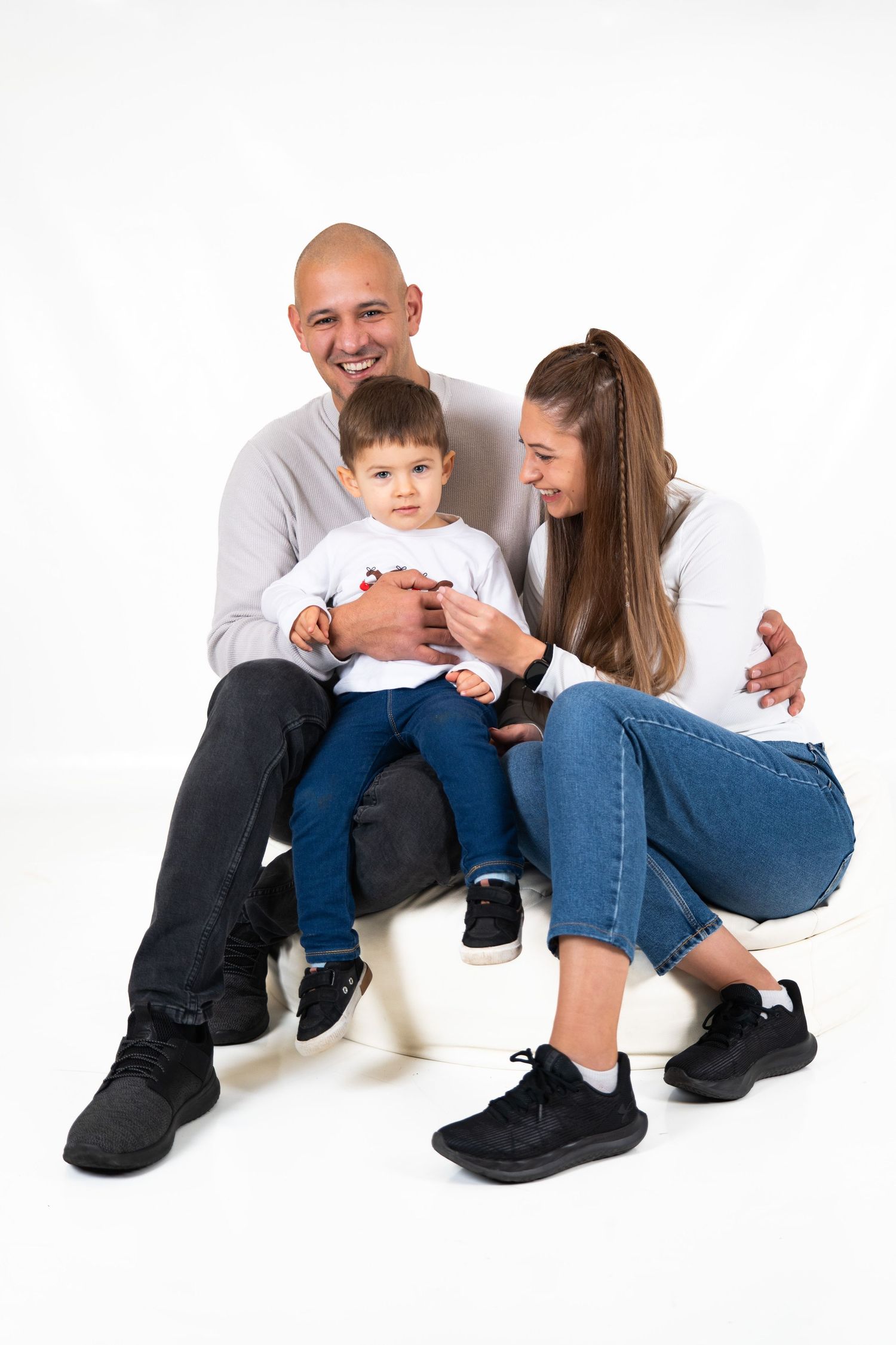 A family sits together on a white background sharing a tender moment in casual clothing.