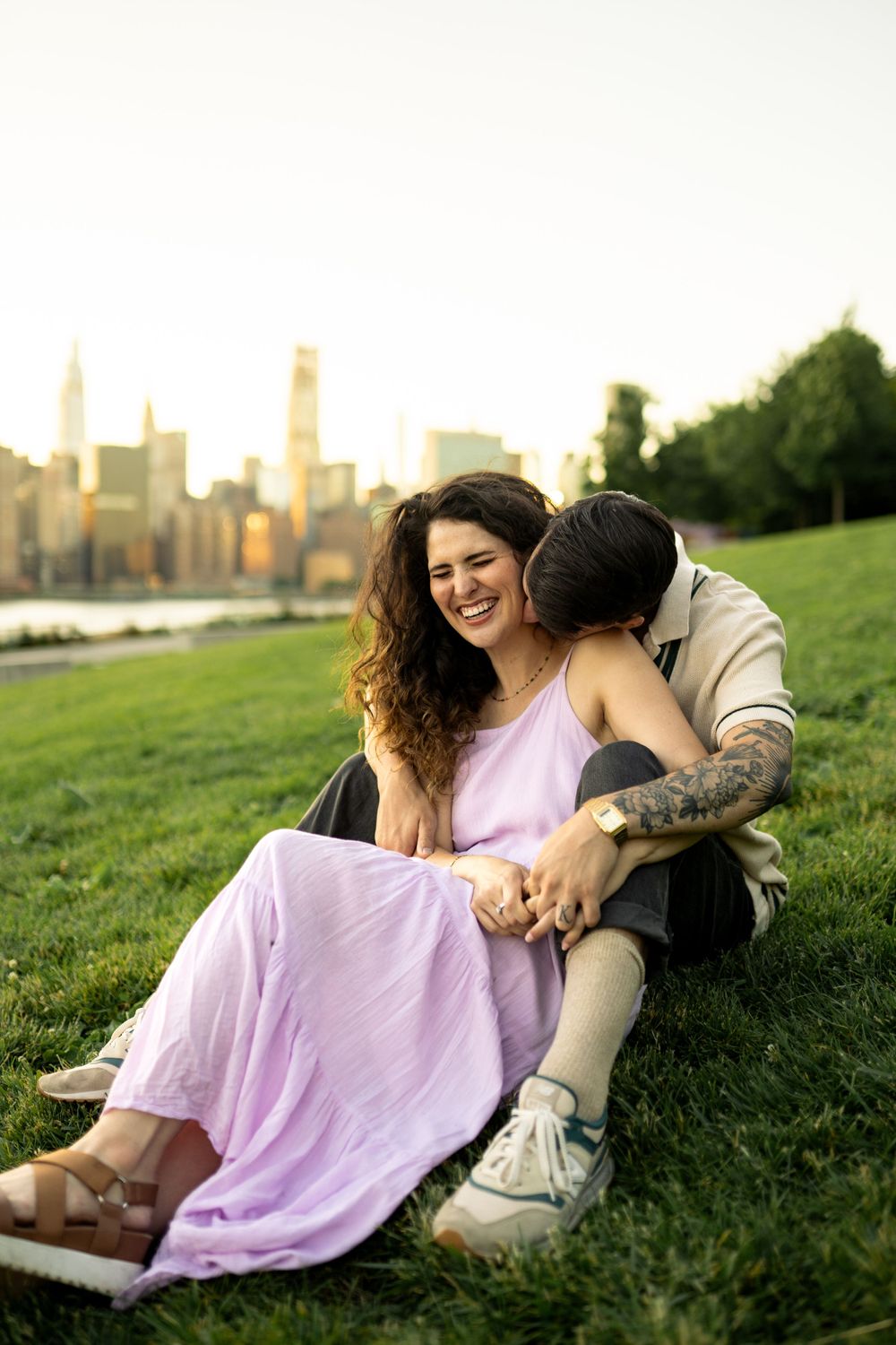 A couple lounges on a grassy hill overlooking the city skyline during golden hour.