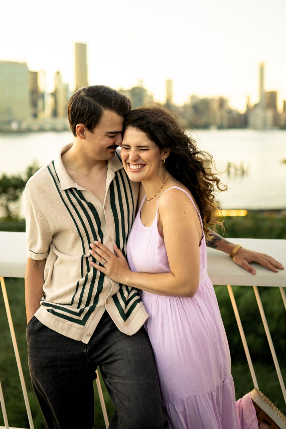 Couple shares laughter and intimate moments along waterfront railing at sunset.