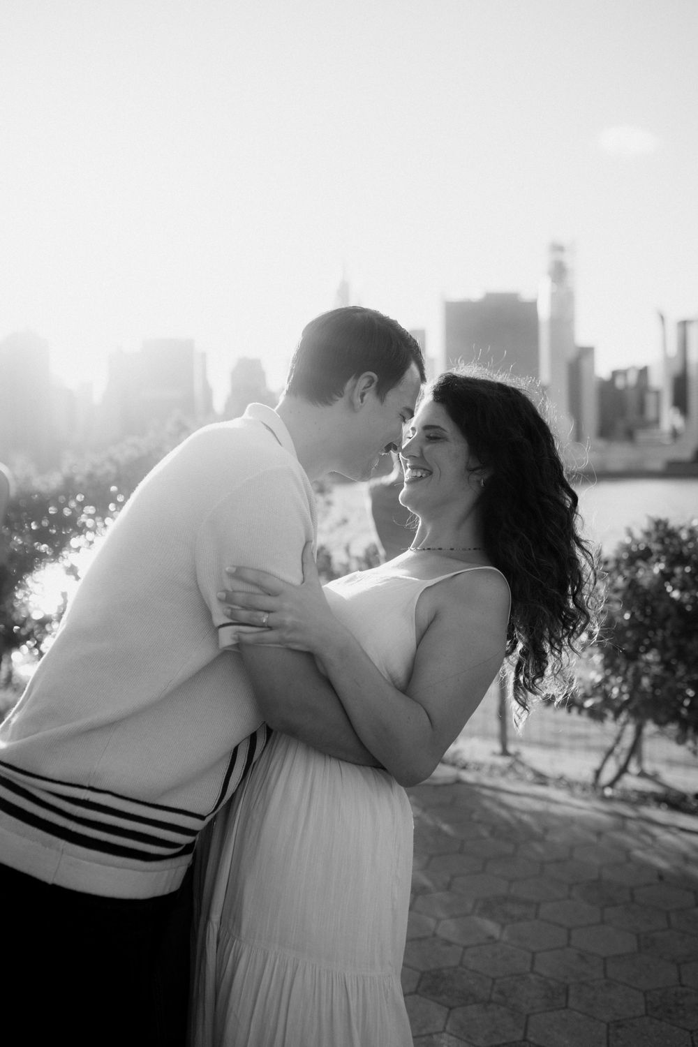 Black and white photo of a couple sharing a romantic moment with city skyline behind them.