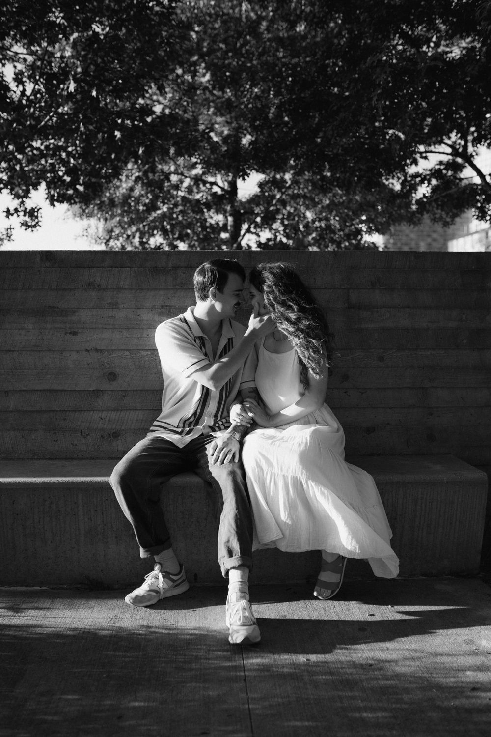 A black and white photo captures a couple's tender moment on a wooden bench.